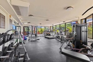Ein Fitnessstudio mit unterschiedlichen Trainingsgeräten, großen Fenstern und Blick auf Grünflächen.