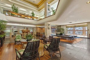 Eine großzügige Lobby mit mehreren Sitzbereichen, einem zentralen Couchtisch und Blick auf die Stadt durch große Fenster.