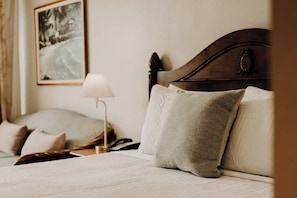A neatly made bed with a white comforter and two pillows, a bedside lamp, and a framed picture on the wall. - Charming Waikiki Studio, Kitchenette+Walk to Beach (Honolulu)