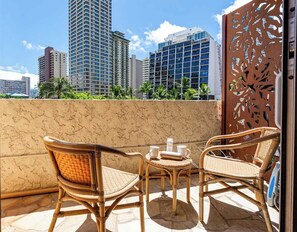 A balcony with wicker furniture, a small table, and a decorative metal screen. - Charming Waikiki Studio, Kitchenette+Walk to Beach (Honolulu)