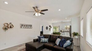 Uma sala de estar moderna com um sofá seccional, um ventilador de teto e uma cozinha ao fundo.