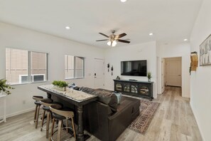 A modern kitchen with a bar area, a dark leather sofa, and a flat-screen TV. - Peaceful 3BR Getaway | Pines, Wildlife, Hiking & Golf (Payson)