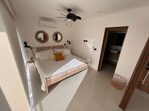 A bedroom with a bed, a ceiling fan, two wall-mounted mirrors, an air conditioning unit, and a doorway leading to a bathroom. - Apartment with a Pool in Puerto Vallarta (Puerto Vallarta)