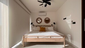 Un dormitorio con una cama de madera, dos unidades de aire acondicionado montadas en la pared, un ventilador de techo y un ventanal grande.