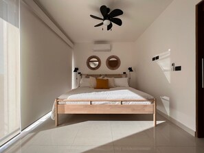 Ein Schlafzimmer mit einem hölzernen Bett, zwei Wand-Klimaanlagen, einem Deckenventilator und einem großen Fenster.