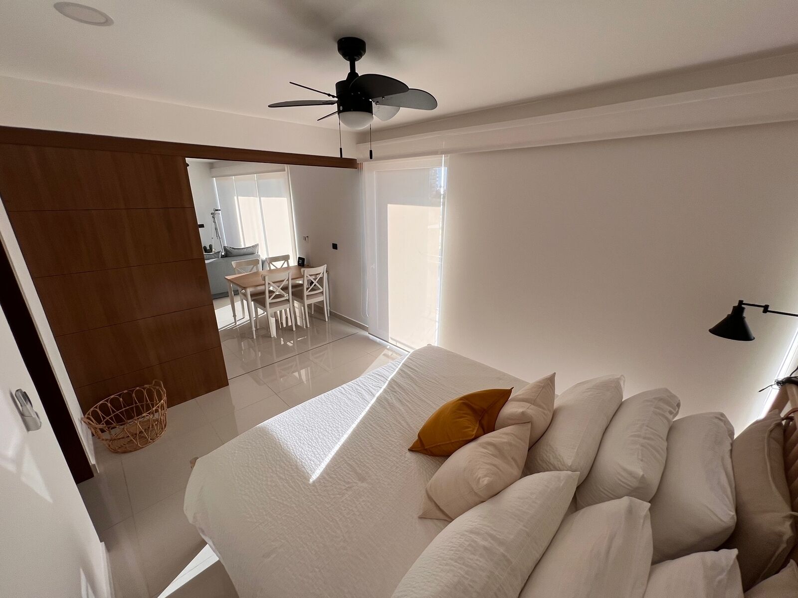 A bedroom with a bed, a ceiling fan, and a view of a dining area.