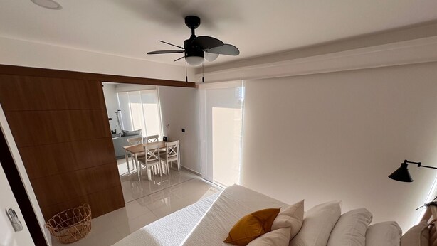 Un dormitorio con cama, ventilador de techo y vista a un comedor.
