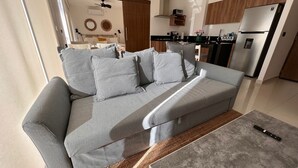 Una sala de estar moderna con un sofá gris, una mesa de centro y una cocina al fondo.