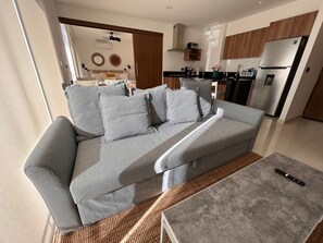 Ein modernes Wohnzimmer mit einem grauen Sofa, einem Couchtisch und einer Küche im Hintergrund.