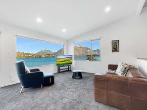 A modern living room with a large window, a sofa, a chair, and a coffee table. - Lakeview Townhouse | Relax Above Queenstown (Queenstown)