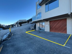 A modern building with a garage door, a parking lot with yellow lines, and a clear sky. - Stunning Lake Views | Sunny Corner Townhouse (Queenstown)