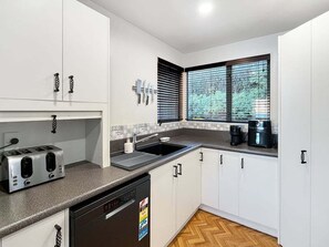 A modern kitchen with white cabinets, a dishwasher, a toaster, and a coffee maker. - Lakeview Townhouse | Relax Above Queenstown (Queenstown)