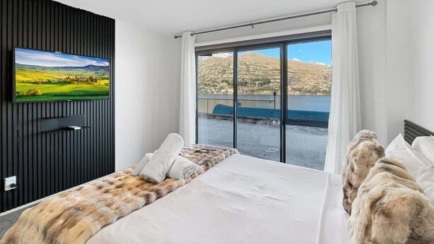 Habitació d'hotel amb llit, televisió penjada a la paret i una finestra gran que ofereix vistes a un paisatge de muntanya.