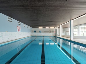 Une piscine aux carreaux bleu clair, un sol carrelé et un plafond orné de lignes horizontales.