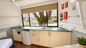 A compact kitchenette with a microwave, sink, and storage cabinets. A window with a view of the outdoors is visible.