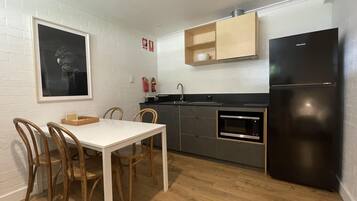 Une cuisine compacte comprenant une table à manger, des chaises, un réfrigérateur noir, un four à micro-ondes et une étagère en bois au-dessus de l’évier.