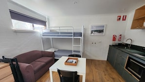 A compact room with bunk beds, a kitchenette, a dining table with a chair, and a sofa. - Tasman Holiday Parks Mount Beauty (Tawonga South)