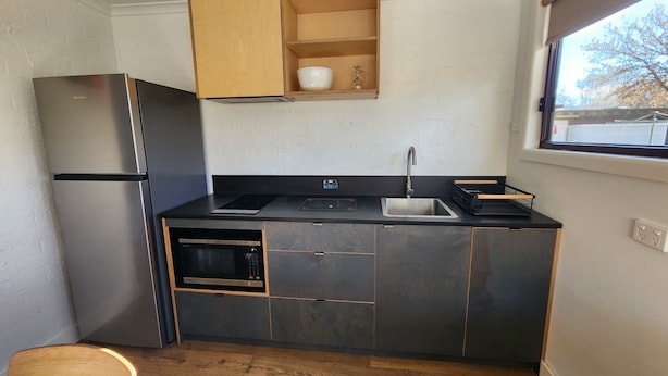 A compact kitchen with a built-in refrigerator, oven, and microwave. There is a wooden cabinet above the sink and a window providing natural light. - Tasman Holiday Parks Mount Beauty (Tawonga South)