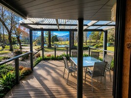 Un espacio al aire libre techado con una mesa y sillas, con vista a un parque con un lago y árboles.