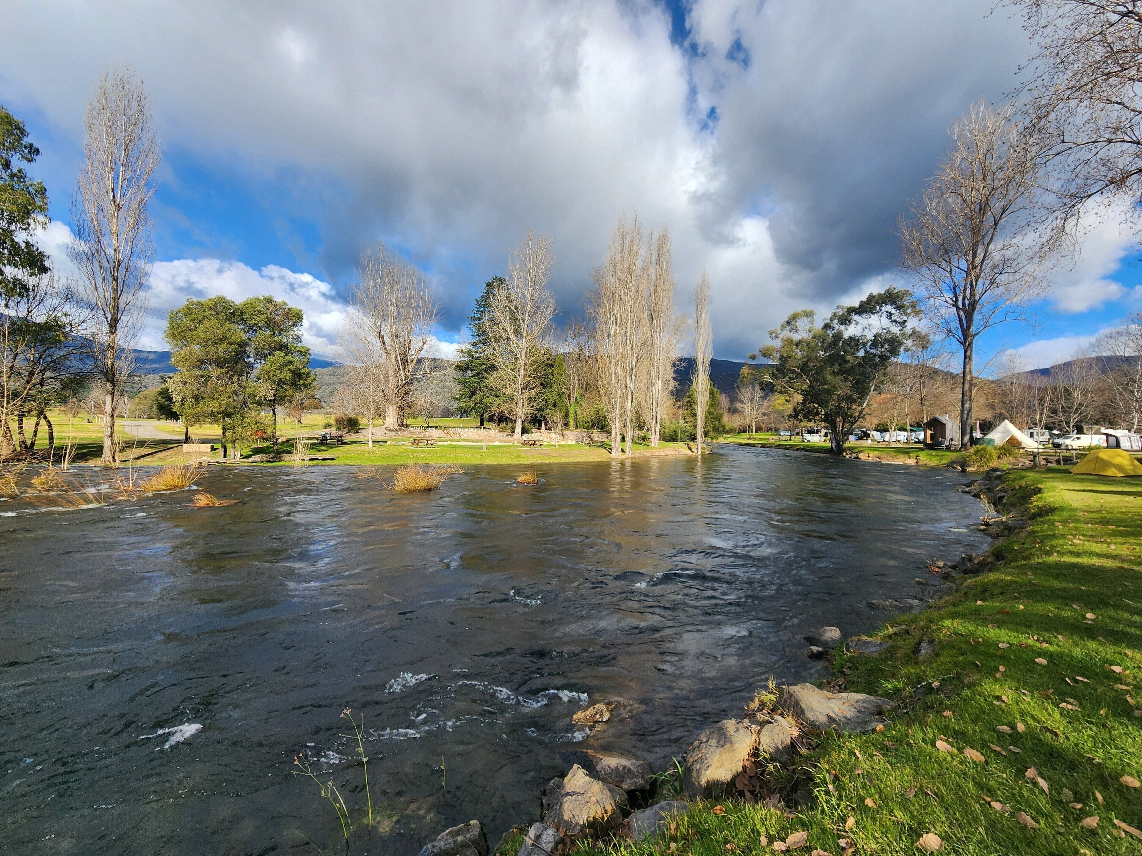 Un río que atraviesa un parque con mesas de picnic y tiendas de campaña.