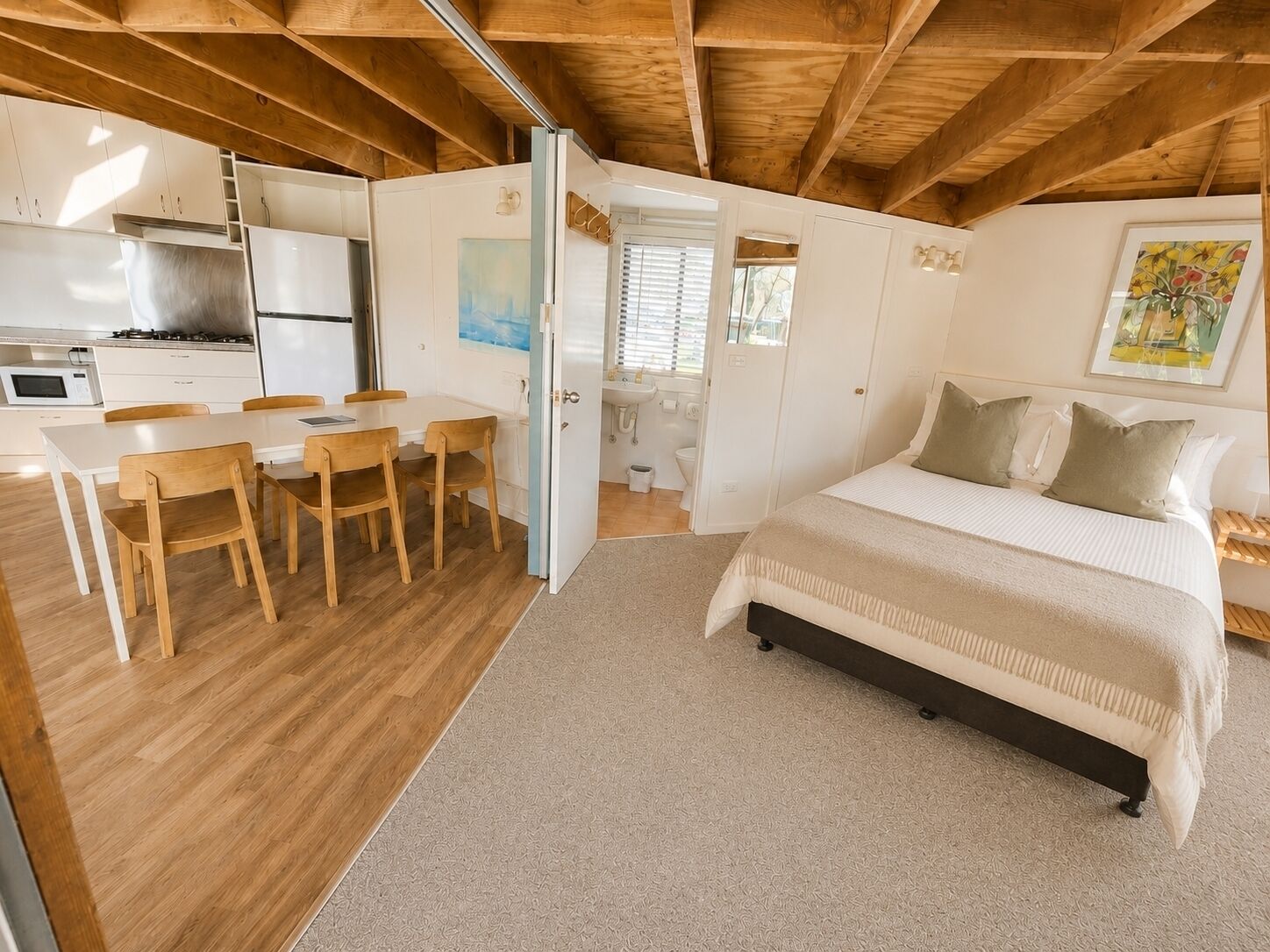 A bedroom with a bed, a desk, chairs, and a kitchen area.