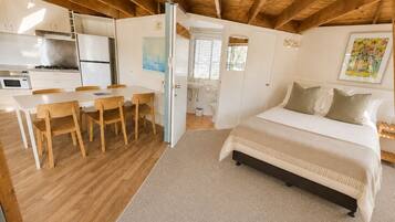 A bedroom with a bed, a desk, chairs, and a kitchen area.