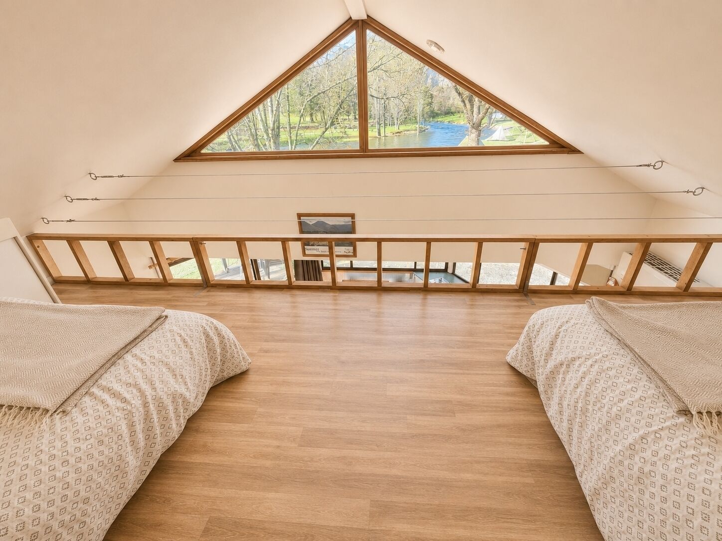 A room with a sloped ceiling, wooden beams, a view of a river, and a small table.