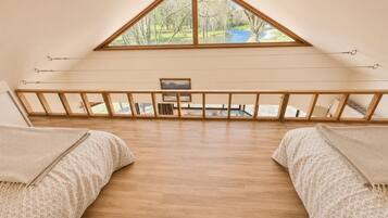 A room with a sloped ceiling, wooden beams, a view of a river, and a small table.