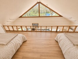 Una habitación con techo inclinado, vigas de madera, vista al río y una pequeña mesa.