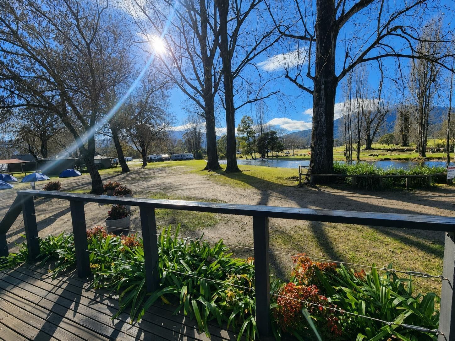 A park with a wooden deck, a lake, and trees.