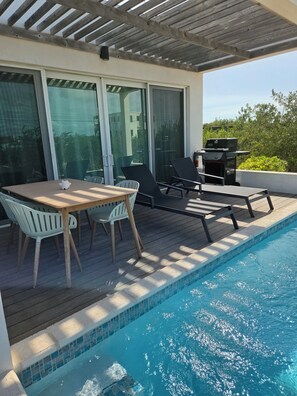 Ein Poolbereich mit Tisch und Stühlen, einem Grill und Blick auf die umliegende Natur.