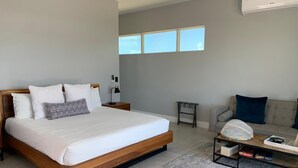 Una habitación de hotel moderna con una cama grande, un sofá, una mesa de centro y una mesita auxiliar.