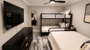 A bedroom with bunk beds, a flat-screen TV, a dresser, and a ceiling fan.