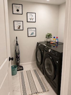A laundry room with a washing machine, a vacuum cleaner, and framed laundry instructions on the wall.