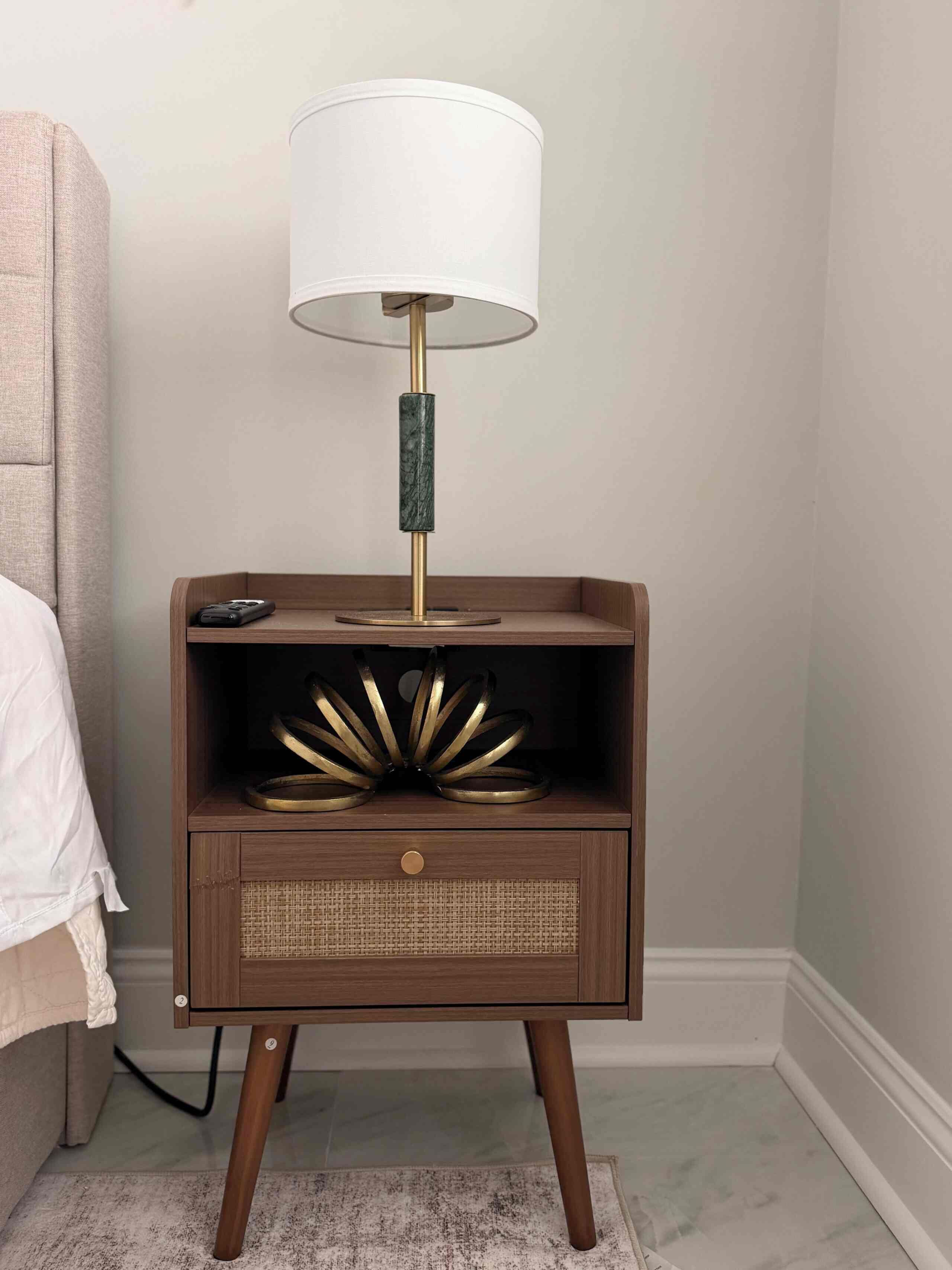 Une table de chevet avec une lampe, un tiroir et une étagère où sont disposés des objets décoratifs.