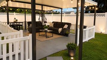 A covered outdoor seating area with a sofa, table, and chairs, surrounded by a white fence.