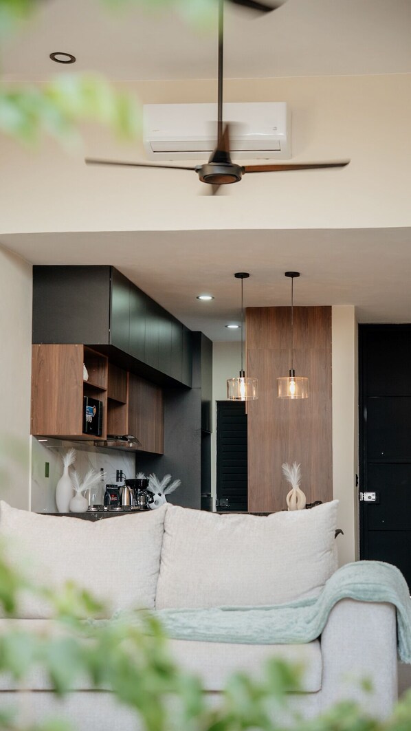 A modern living room with a sofa, a ceiling fan, and pendant lights.