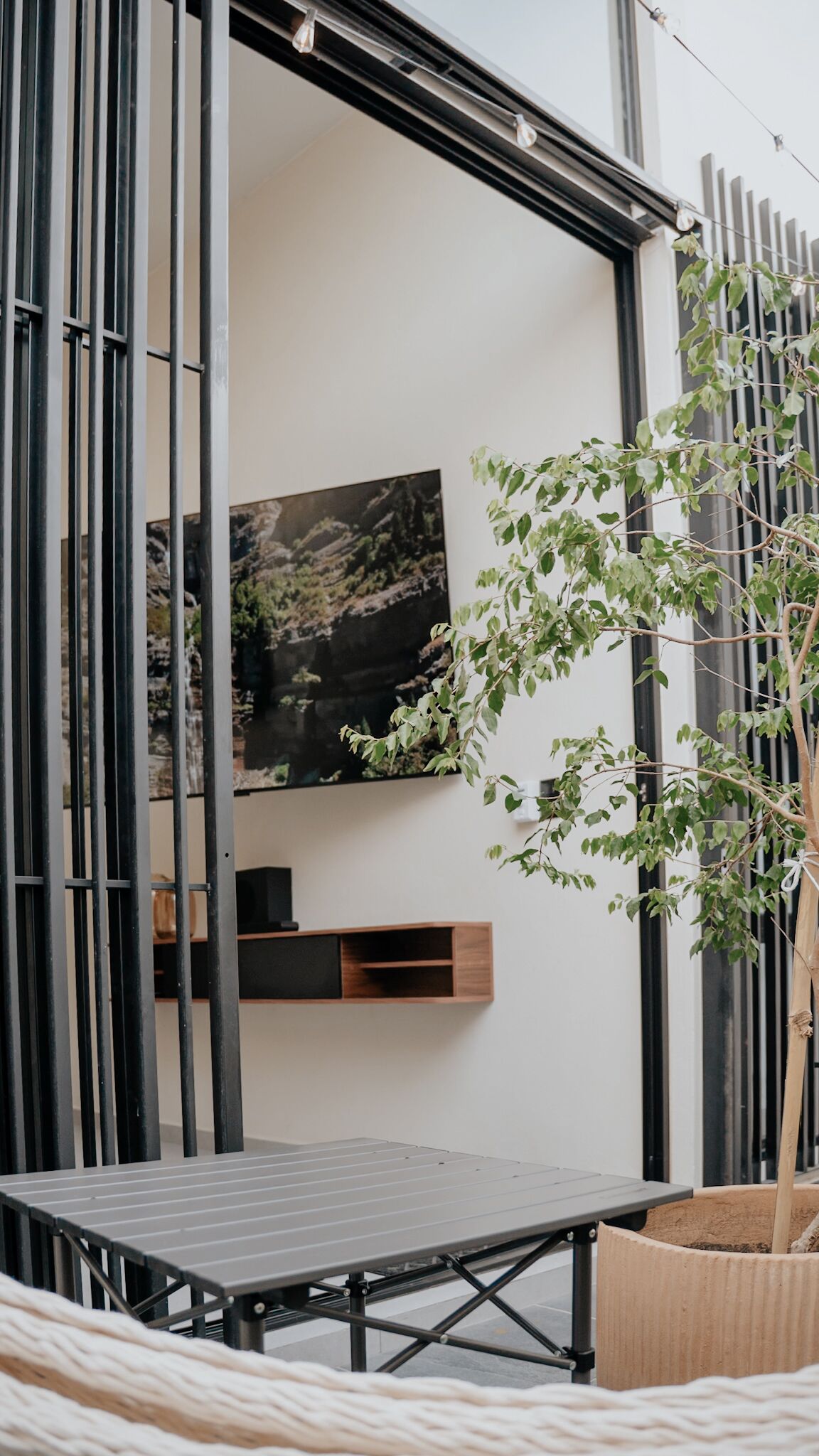 A modern interior with a metal-framed table, a wall-mounted shelf, and a potted plant.