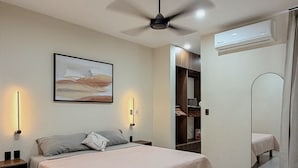 Une chambre à coucher comprenant un lit, un ventilateur de plafond, un climatiseur fixé au mur et un grand miroir.
