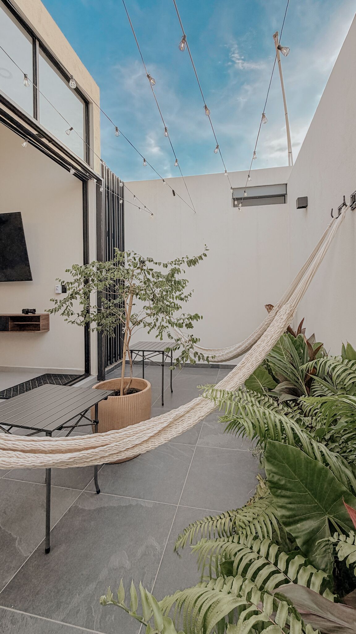 A modern outdoor patio with a hammock, a small table, and potted plants.