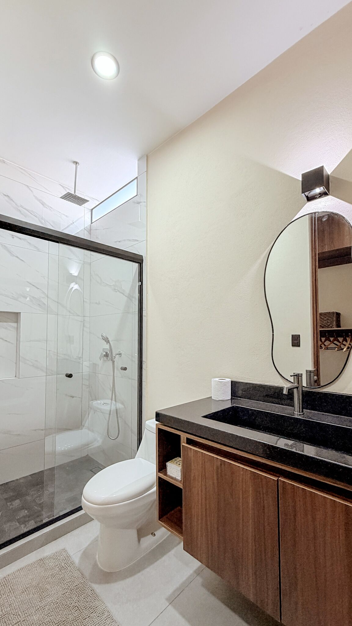 A modern bathroom with a glass-enclosed shower, a toilet, and a vanity with a mirror.