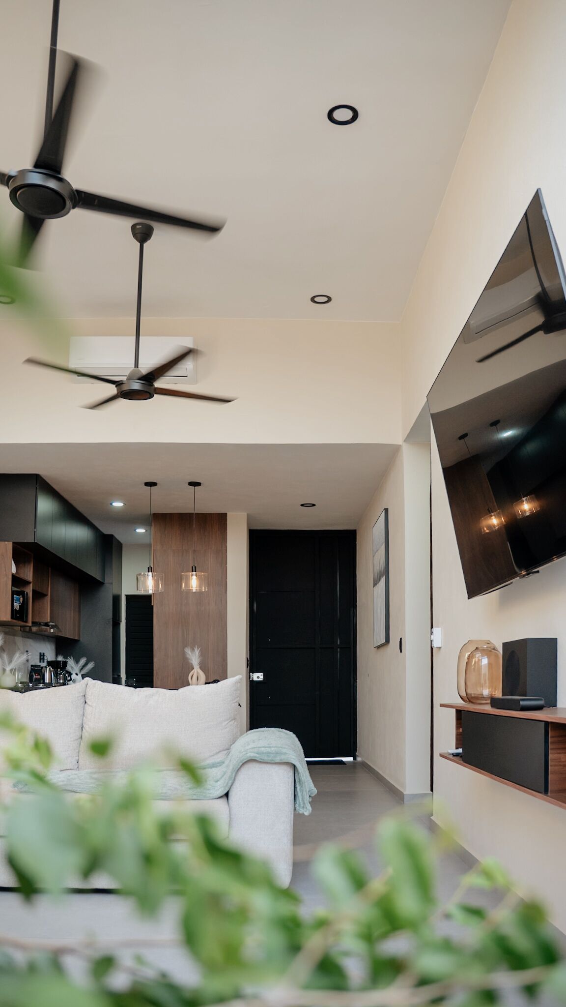 A modern living room with a ceiling fan, a flat-screen TV mounted on the wall, and a sofa.