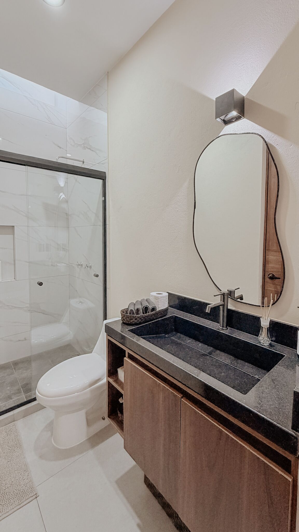 Un baño con cabina de ducha de vidrio, inodoro, tocador con lavamanos y espejo.
