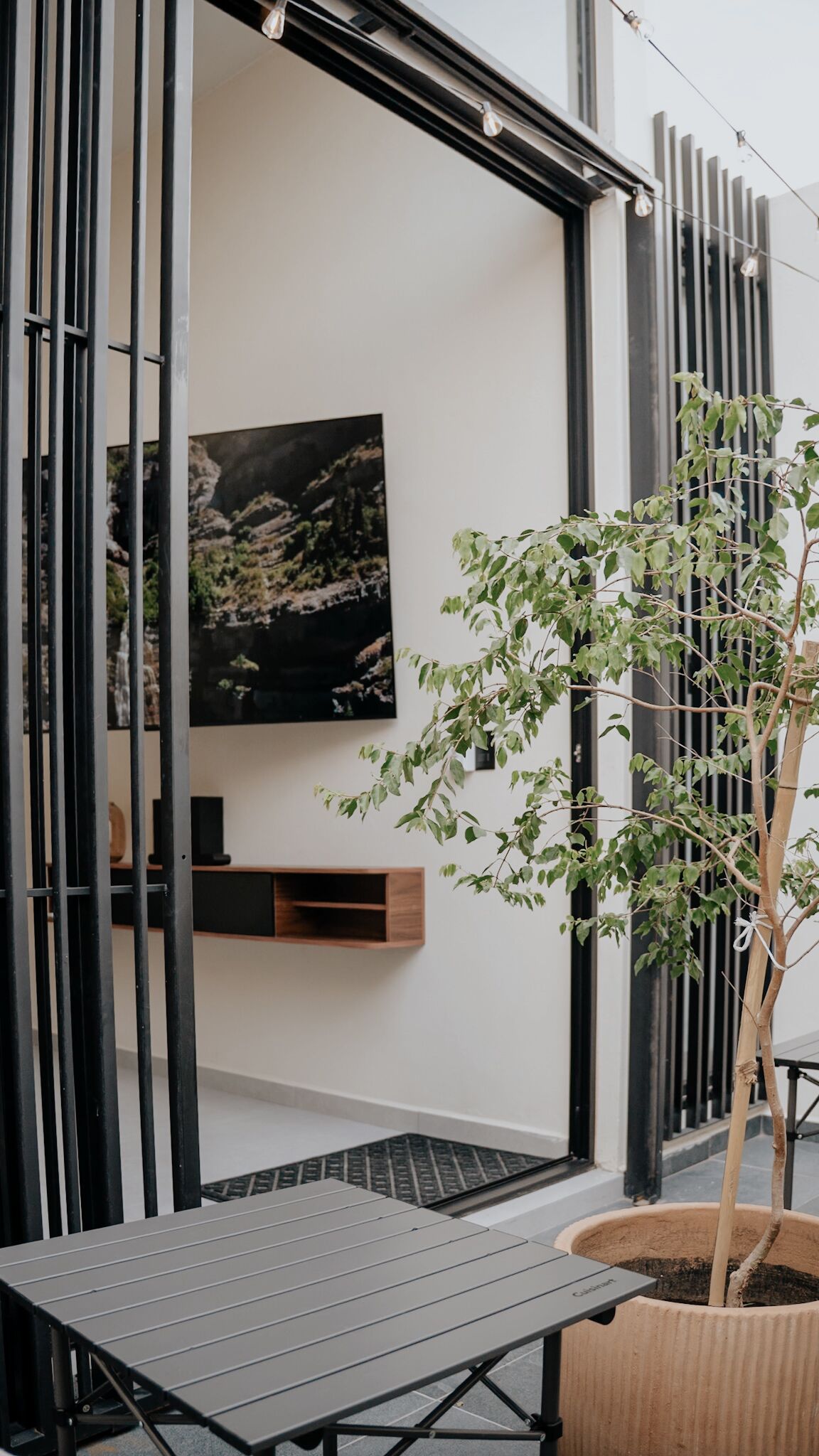 Un interior moderno con diseño minimalista, que incluye un ventanal con marco negro, un televisor montado en la pared y una planta en maceta.