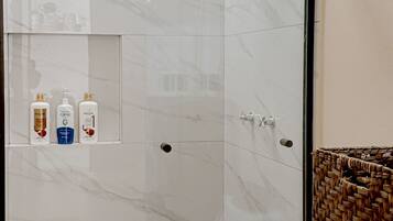 Un baño moderno con ducha de vidrio, inodoro blanco y repisa con artículos de aseo.