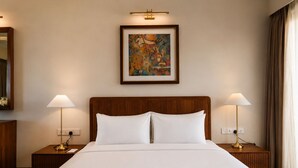 A hotel room with a large bed, two bedside lamps, a framed artwork above the bed, and a mirror on the left wall.