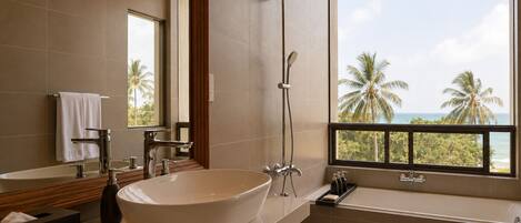 Un baño moderno con una bañera independiente, zona de ducha separada y un amplio ventanal con vistas a palmeras y al océano.