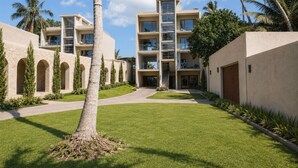 A modern multi-story hotel with a central courtyard, palm trees, and a clear sky.