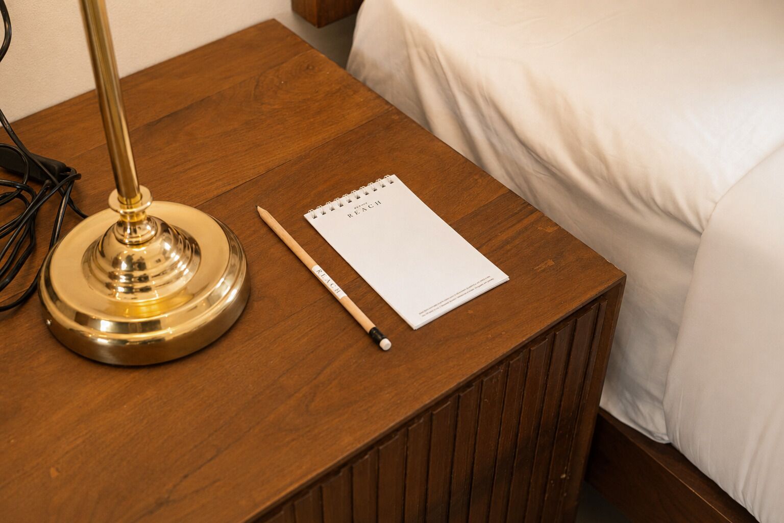 A wooden bedside table with a lamp, a notepad, and a pen.