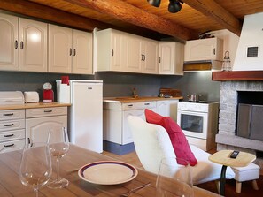 A kitchen with white cabinets, a wooden countertop, a stove, and a dining area with a table set for two. - Rustico Grace by Interhome (Malvaglia)